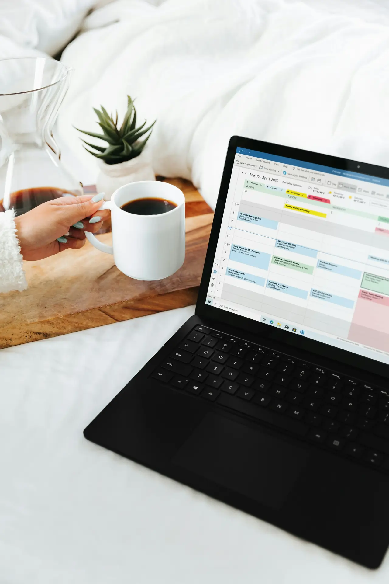 A person holding a coffee mug in front of a laptop showing a weekly calendar