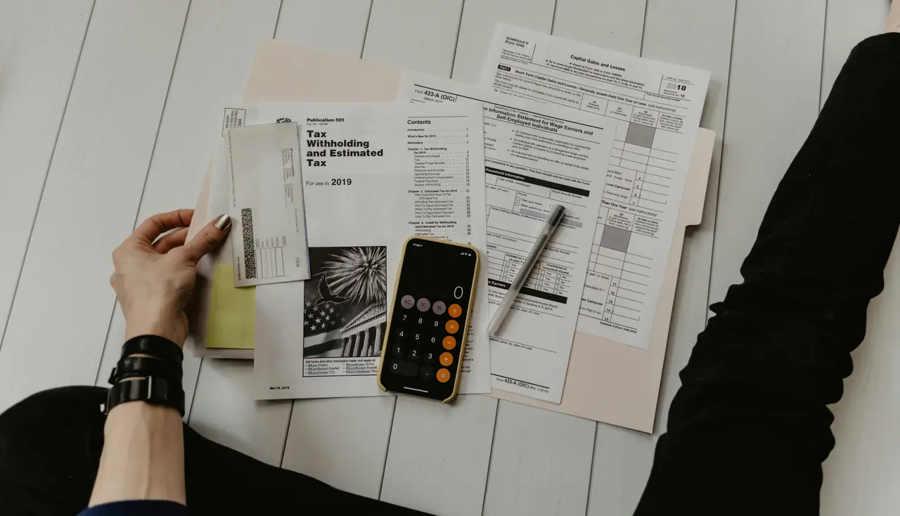 Hands sorting household paperwork beside a calculator, pen and phone