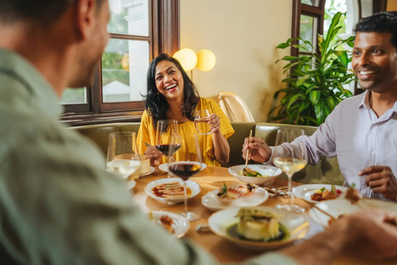 Three friends laughing over dinner at a restaurant table