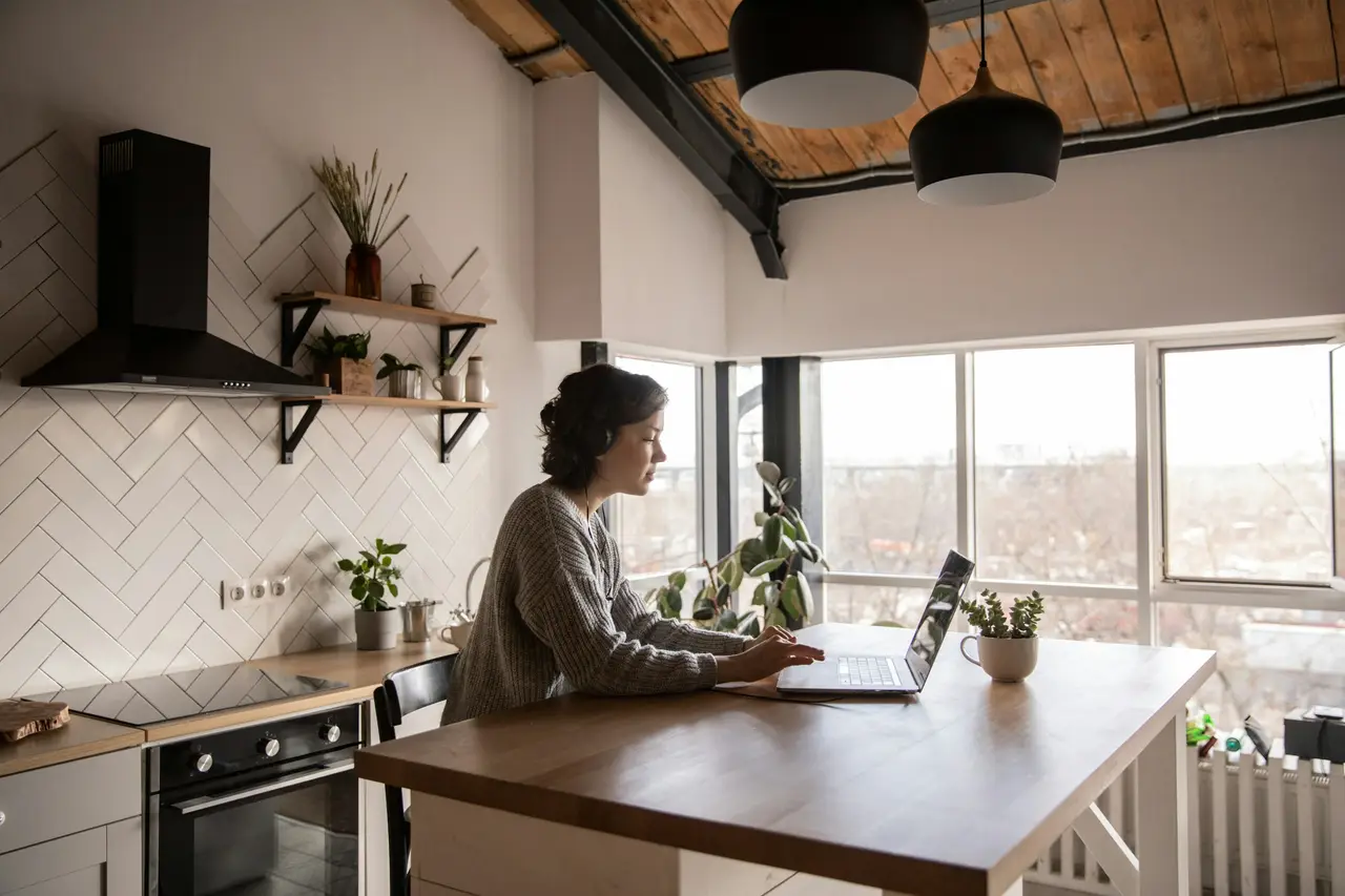 A man working on a laptop at a kitchen table in a bright, open-plan home