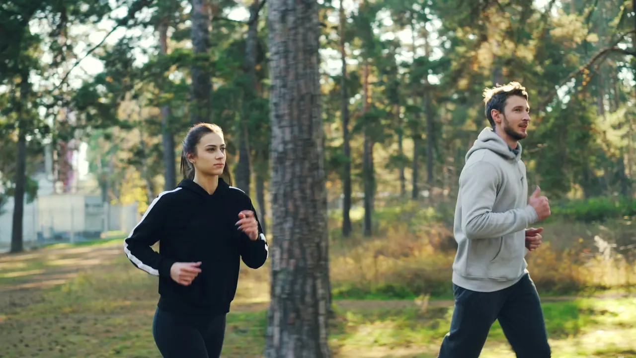 A man and a woman jogging together along a path in a wooded park