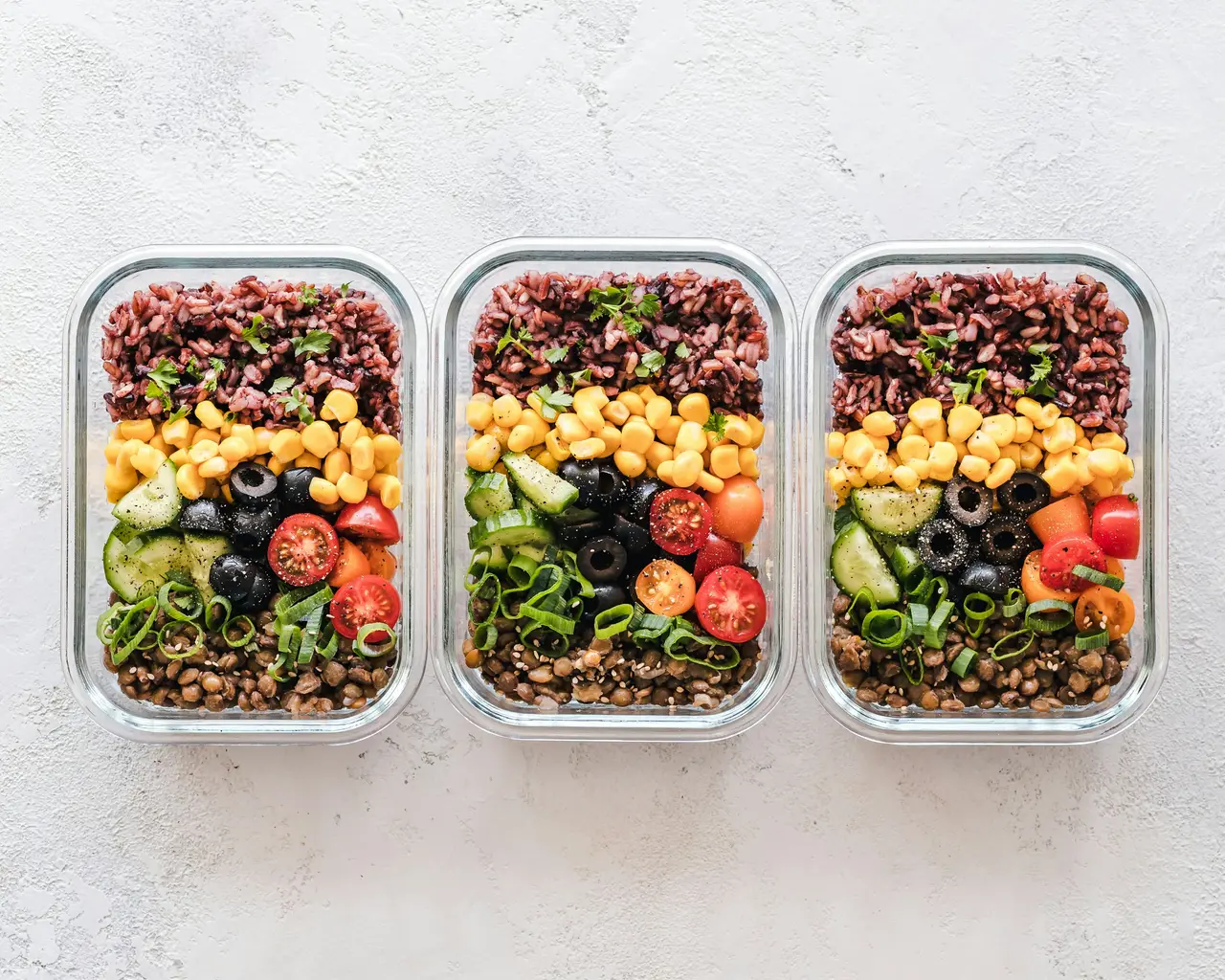 Three glass meal-prep containers with grains, vegetables and lentils